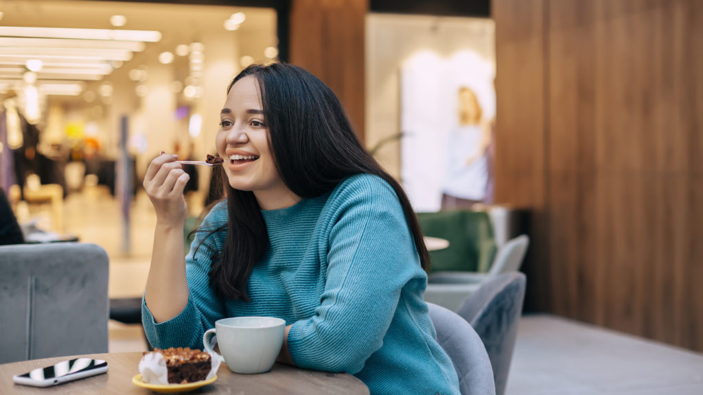 Beautiful plus size woman eating dessert with coffe while resting in cafe inside city mall